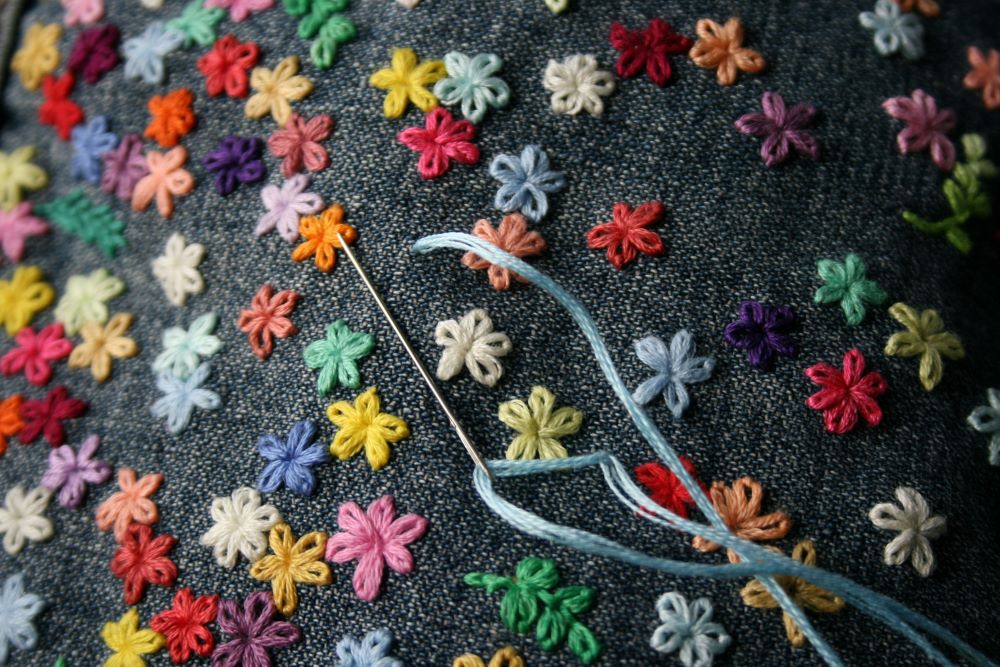close up of colorful flowers being embroidered on to blue fabric