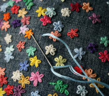 close up of colorful flowers being embroidered on to blue fabric