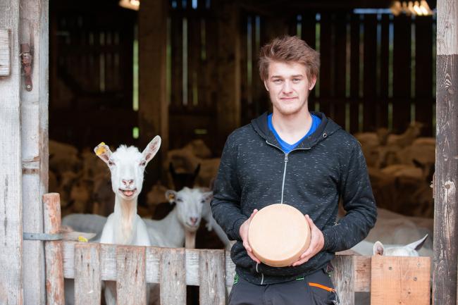 Man holding goat cheese standing in front of his goats